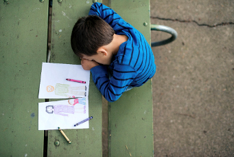 Child sitting alone with head down over a drawing
