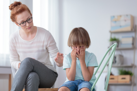 A therapist sitting with a child who is covering their face with their hands