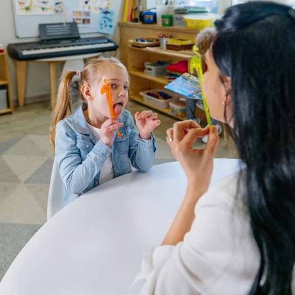A speech therapist working with a child using therapy tools at a table